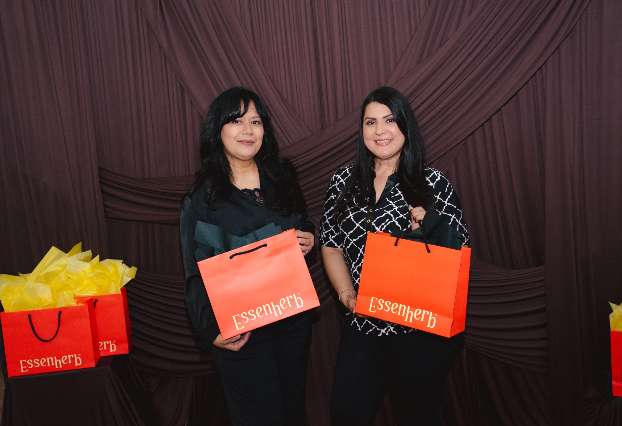 Wide photobooth shot of two guests with their goodie bags against the brown velvet backdrop