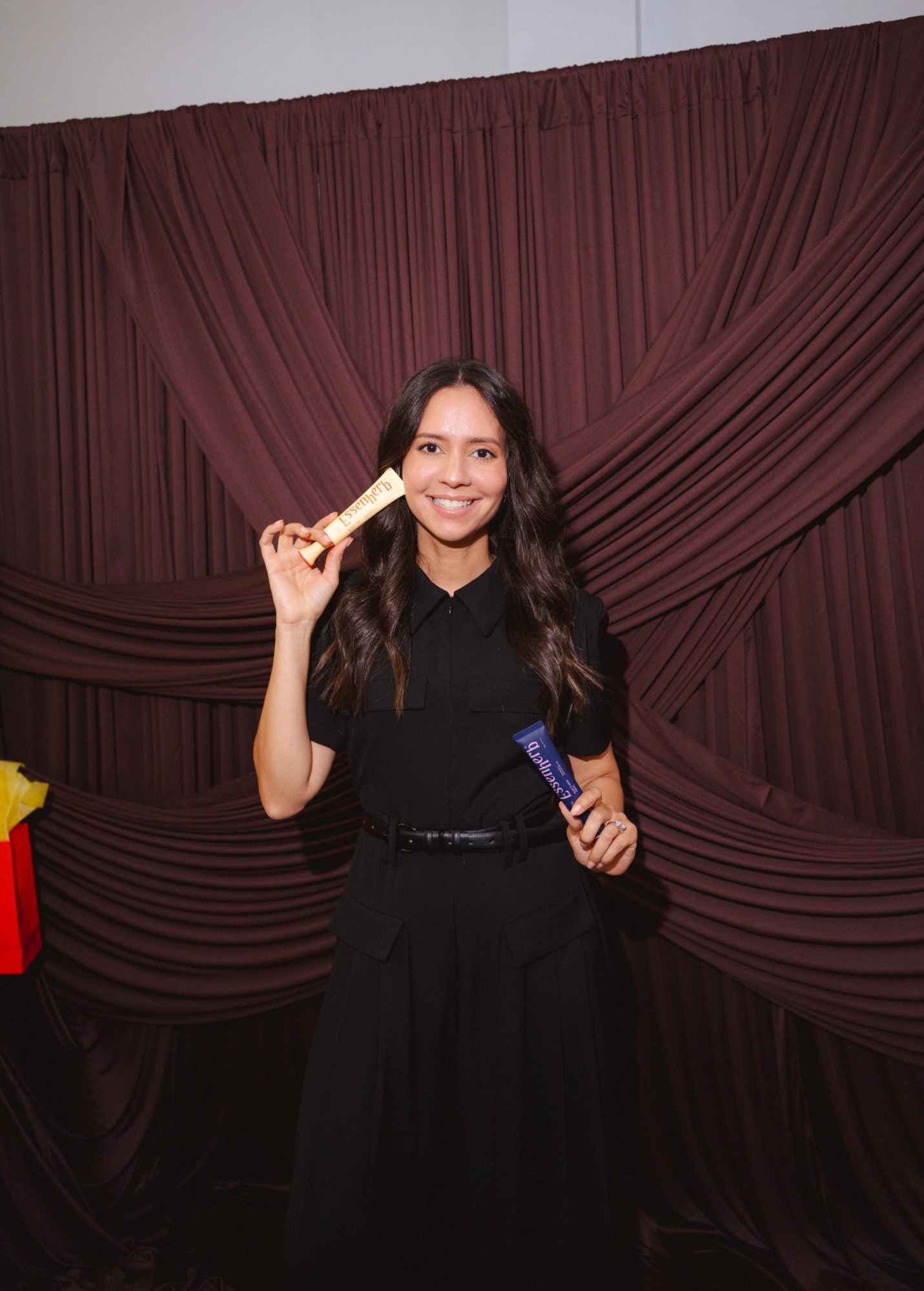 Guest posing with two products at the photobooth backdrop