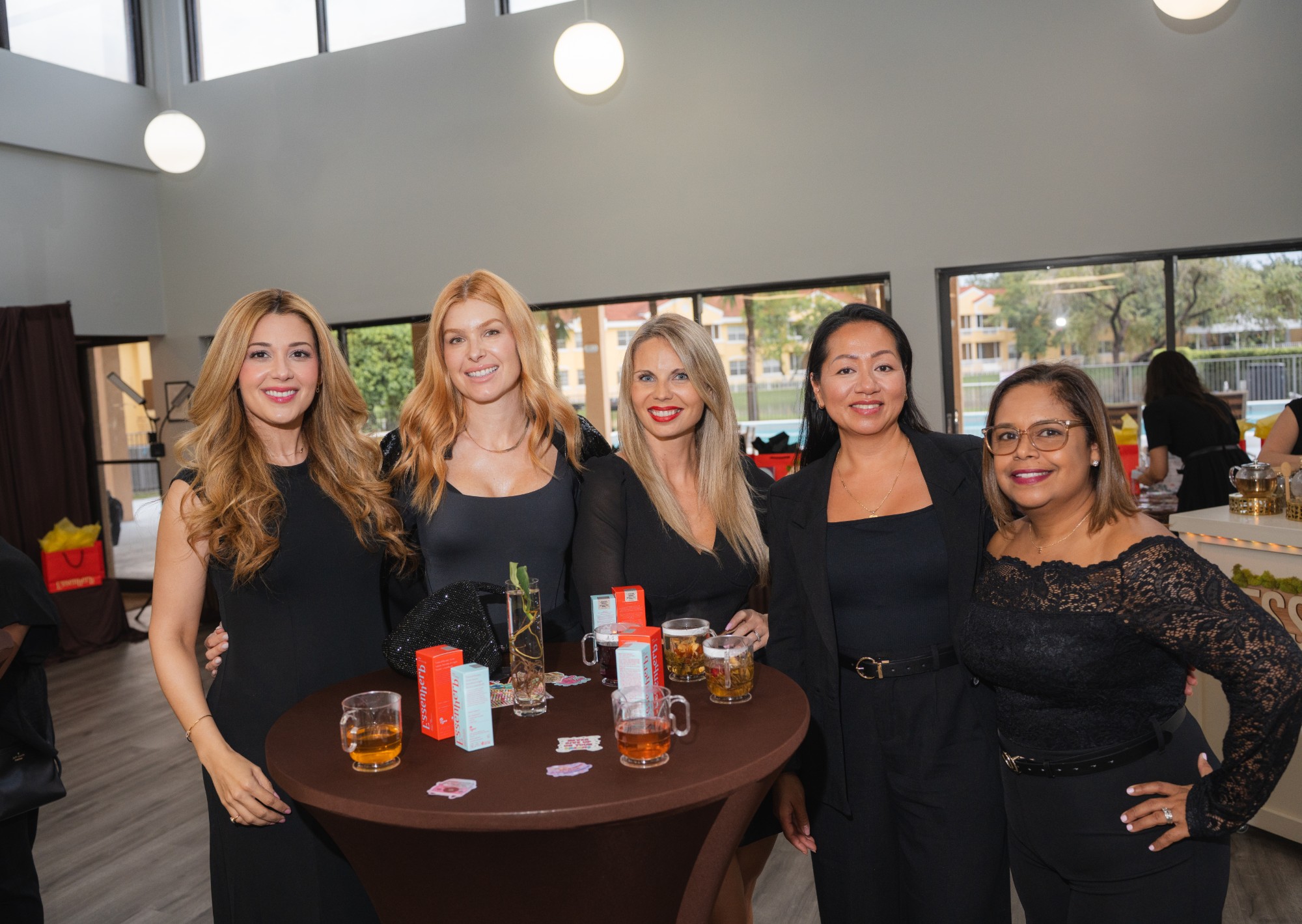 Five guests posing together at a cocktail table with tea and products