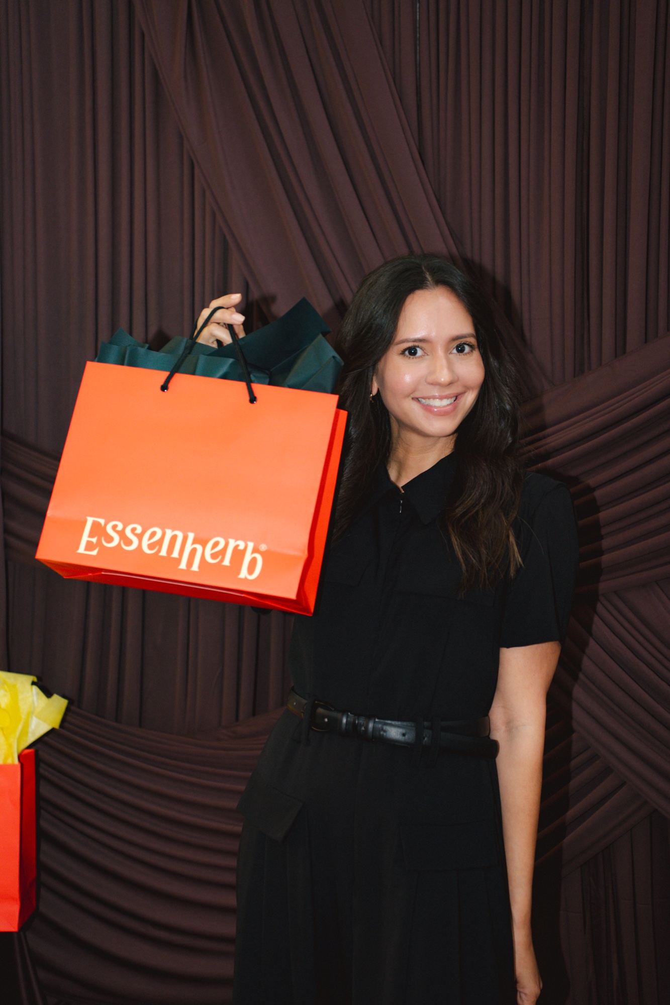 Guest posing at the photobooth backdrop with an Essenherb gift bag