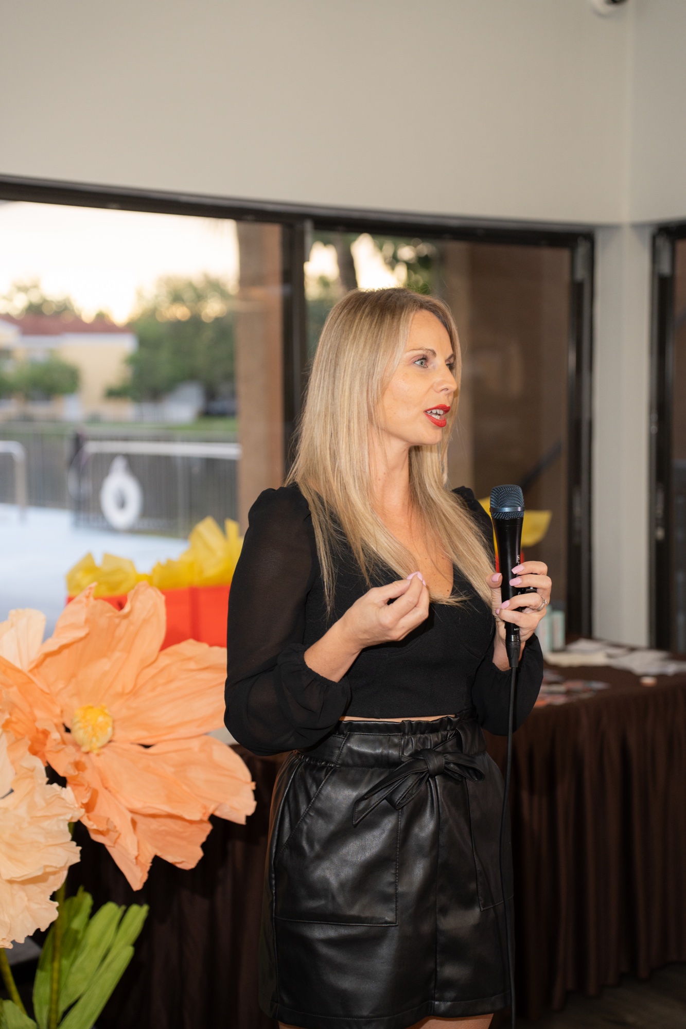 Host mid-speech with the giant paper flower in view